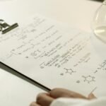 A close-up view of handwritten chemical formulas on a clipboard in a lab setting.